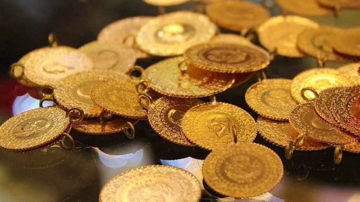 Pile of shiny gold coins/medallions with holes scattered on a dark reflective surface, catching light.